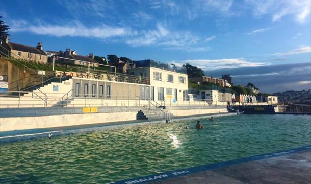 A 1920s simple lido building - mostly single storey changing rooms - alongside a triangular pool.