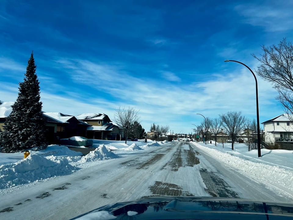 View of a snow covered road with sidewalks and front yards covered with snow.