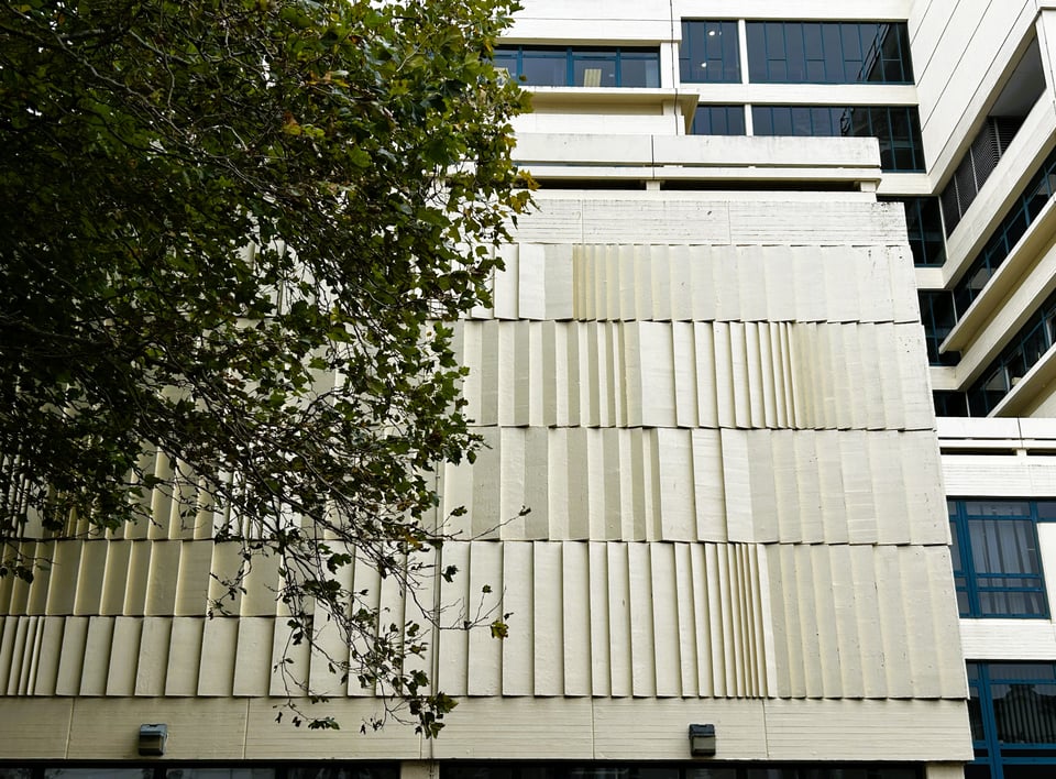 A two storey blind wall with no windows. The concrete has been cast to form several rows of wedges at differing angles. It is, of course, painted cream.