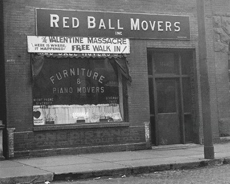Photo of the front of the building in the 1930s. The sign says Red Ball Movers and underneath there is another sign that says "The Valentine Massacre. Here Is Where it Happened" "Free Walk In"