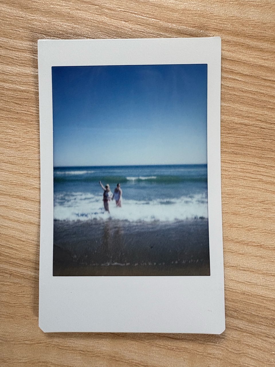 A blurry Polaroid of two people standing in the ocean waves, one of them holding a baby and is waving back