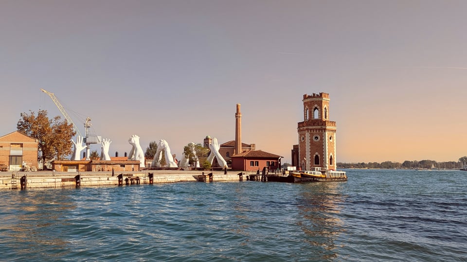 Overlooking the Building Bridges art installation (5 pairs of joined hands in different positions). The sky is a dramatic grey-golden color, the water different shades of blue.