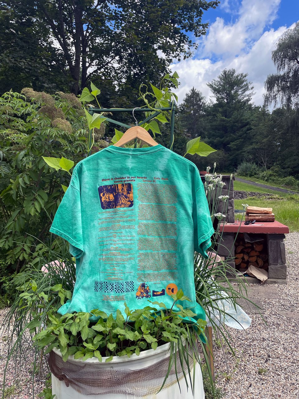 the back of an ALLORA t-shirt in an herb barrel