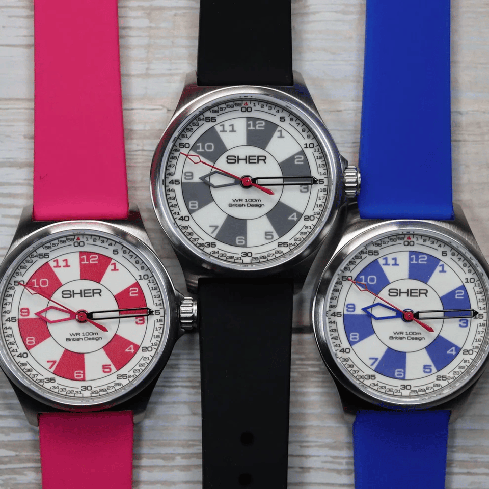 A photo of three Sher Kids Watches. Their faces are divided into alternating colored-and-white chunks for each hour; it has a bold and crisp look. The watch on the far left is red, with red chunks on the watch face; the middle watch is black, and the far right is blue