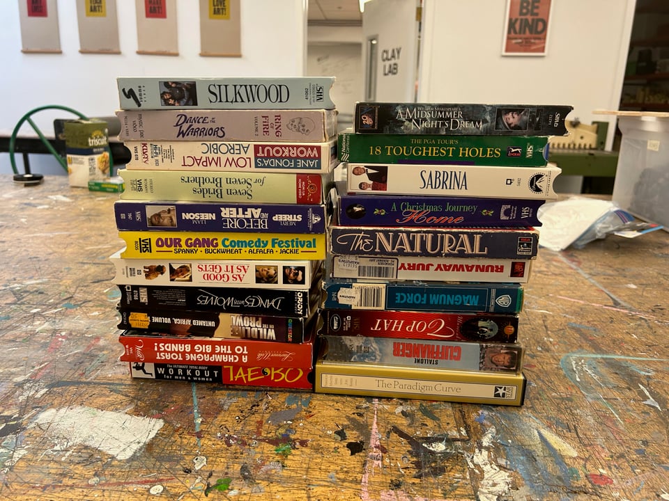 A stack of VHS tapes on a messy counter