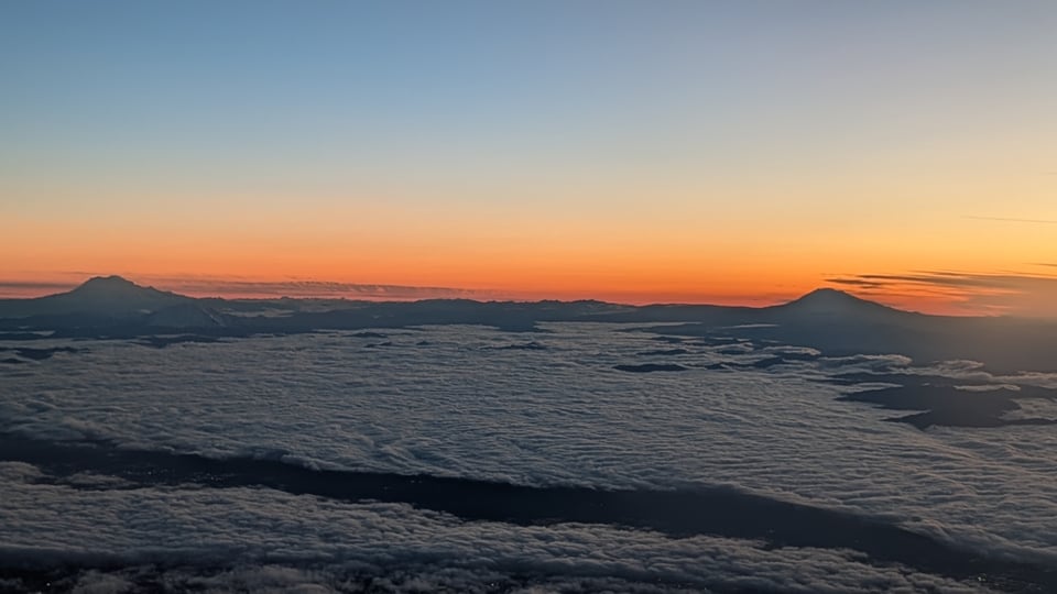 Two mountains and clouds under a blue and orange sky