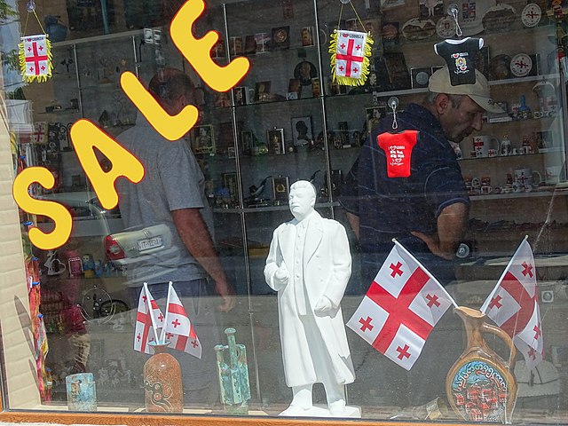 Shopfront featuring a statue of Stalin, Georgian flags, and various knick-knacks. The word SALE is emblazoned in garish yellow.