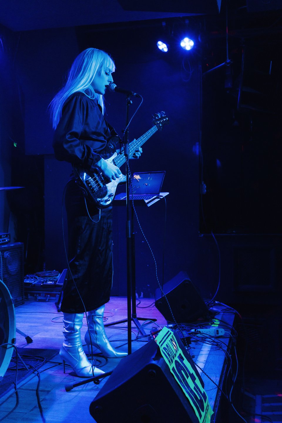 Zir Indigo (Lotus) plays bass /sings on stage at Piano. We see a poster from the fundraiser in the bottom, and their laptop screen is a picture of dolphins.