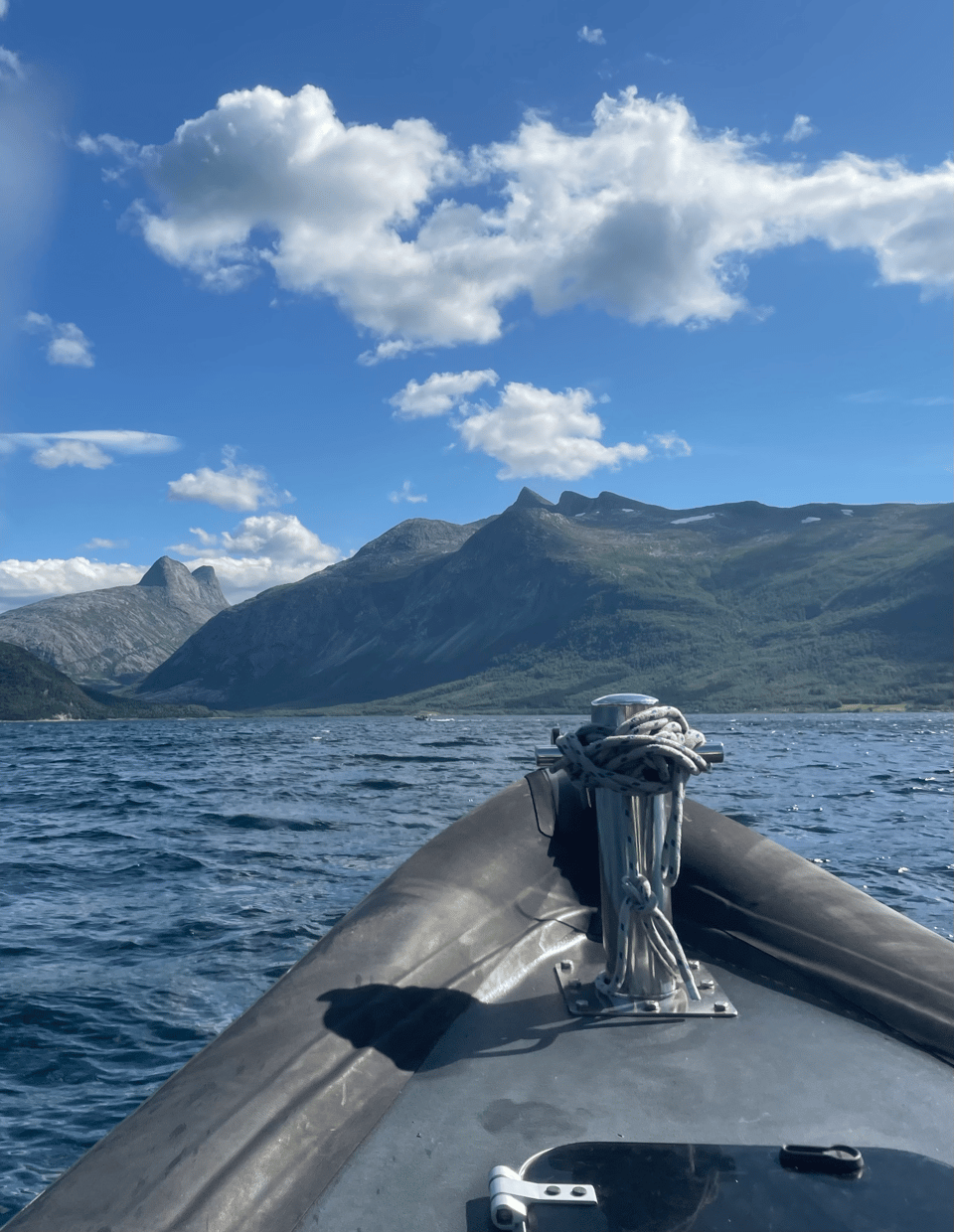 The tip of a small boat splashing toward a rocky mountain range