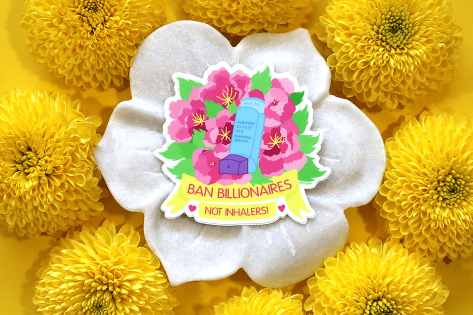 A sticker of a colorful floral art design behind a blue and purple inhaler that has the label "Albuterol Sulfate HFA Inhalation Aerosol" and the expiration date "Aug 20" on it. The floral design shows several big, pink peonies with yellow stamens and bright green leaves. Underneath the design is a yellow banner with pink text on it that reads, "Ban Billionaires, Not Inhalers!" in all caps and two pink hearts on either side. The sticker is on a round piece of marble, resting on a mossy green background, styled with pieces of wood and a bright yellow mum flower.