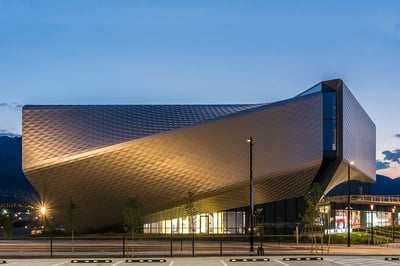 A building made of swooping metal covered with triangles, looming over an entrance plaza.