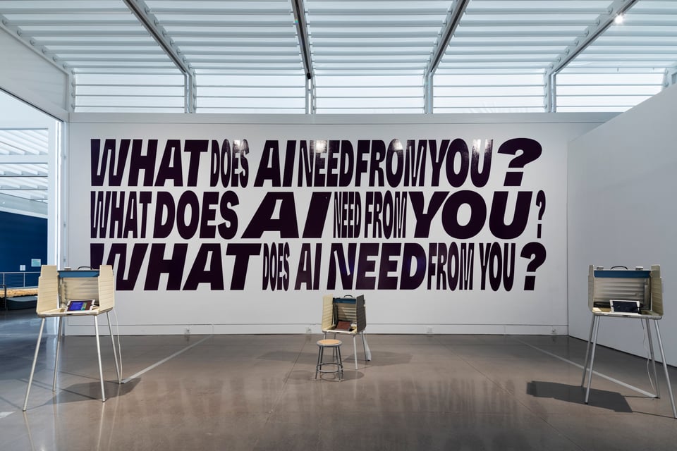 A wall with large text that reads “What does AI need from you?” three times, stacked vertically. With each question, the emphasis is on different words.