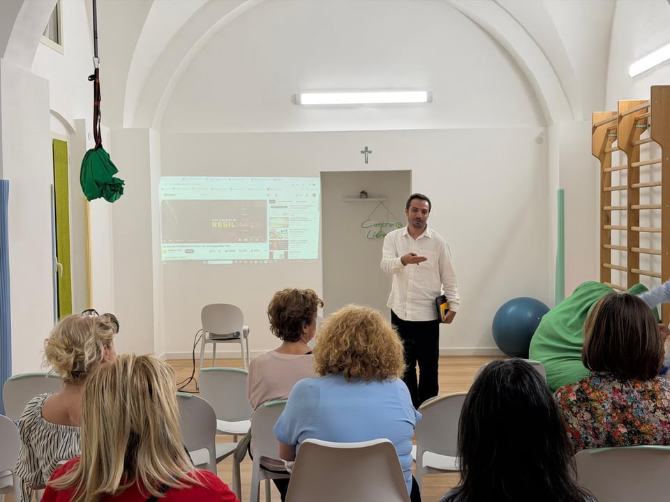 A photo of a Palestinian man speaking to a group of people in a large room. He's mid-speech.