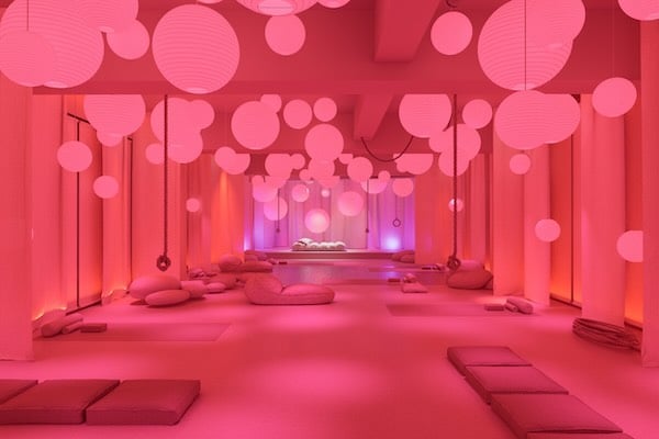 Una sala iluminada de rosa o magenta, con distintos asientos blandos en el suelo y con lámparas redondas de diversos tamaños distribuidas irregularmente por el techo.