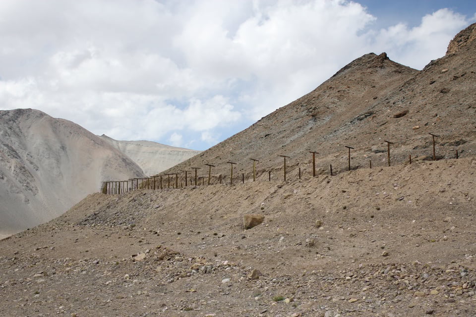 Photograph of a barbed wire fence running across a barren, rocky hillside.