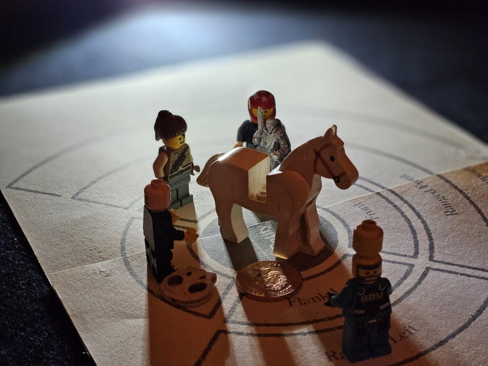Four Lego mini figures and a 3D printed miniature surround a Lego horsie, all arranged on a printed-out tactical battle grid and dramatically back-lit