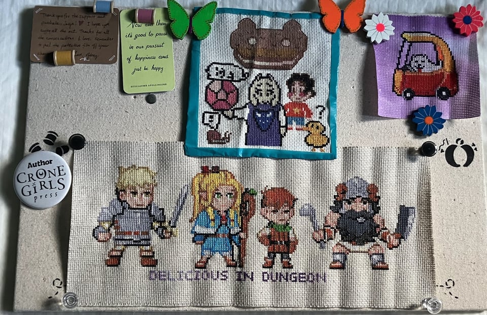 Bulletin board with cross-stitches from my friend Bettina Levy featuring characters from Steven Universe, Dungeon Meshi, and Undertale