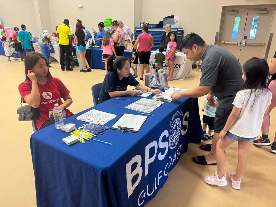 Two Asian American young women sitting at a table with a blue BPSOS Gulf Coast tablecloth speak to an Asian family