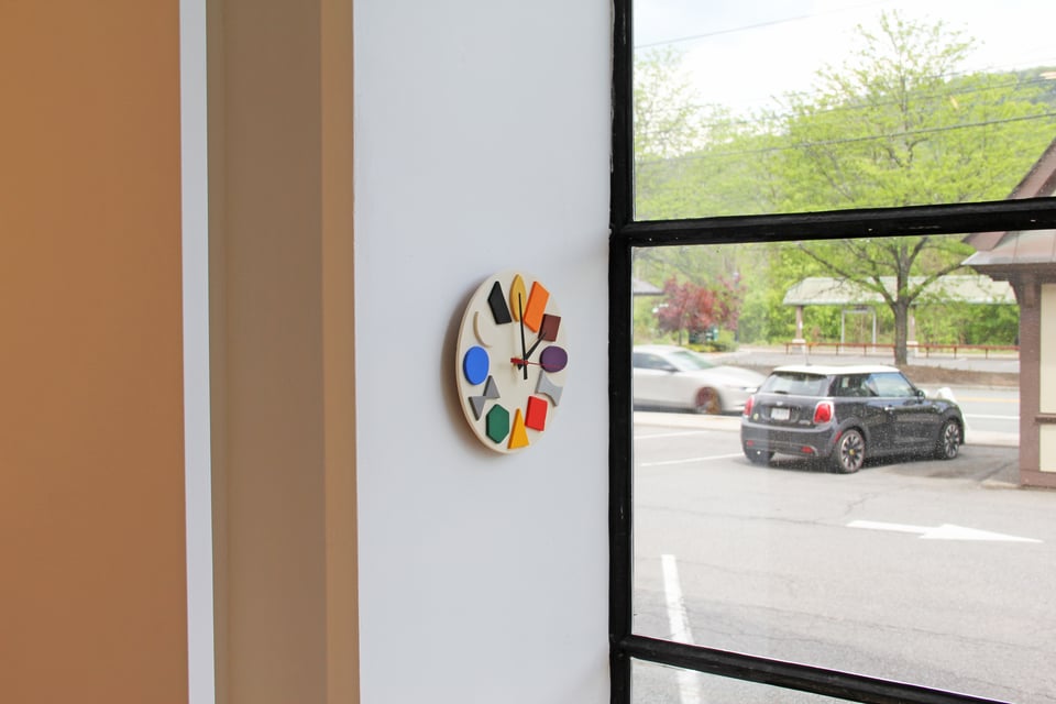 clock with colorful shapes for numbers on thin wall beside window