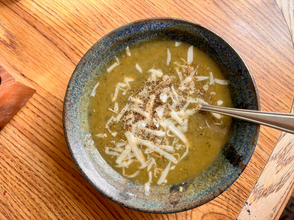 A Birds Eye view of a bowl of greens blended soup with parmesan and pepper on top