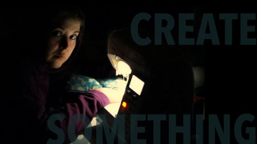 a person sits in front of a sewing machine, looking into the camera with an inscrutable expression, face illuminated by the machine's lamp in an otherwise dark room; overlaid text reads "create something"