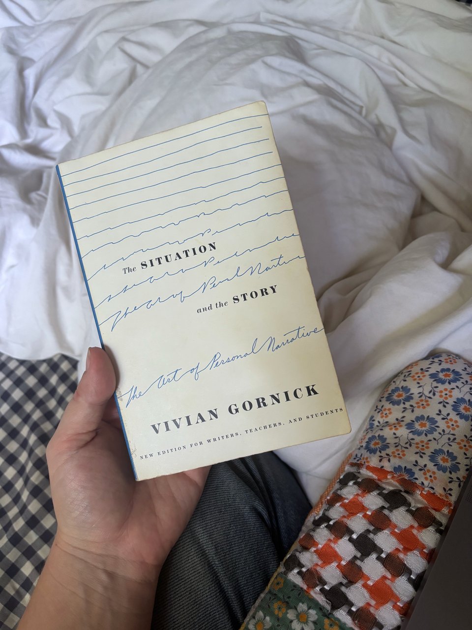 my left hand holding "The Situation and the Story" by Vivian Gornick above my white and blue gingham bedding