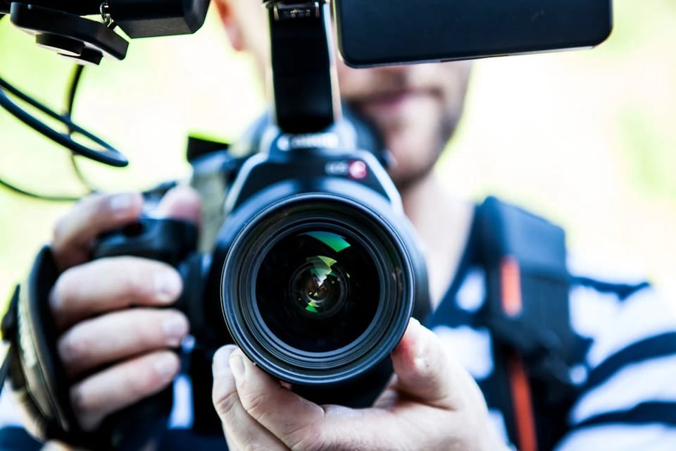 A man pointing a camera right at us. His lower face is visible
