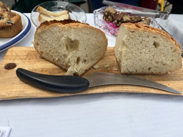 A loaf of bread sliced in half so you can see all the yummy air bubbles. It rests on a table with a knife and looks delicious.