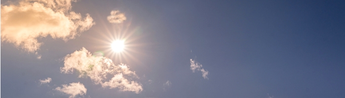 A bright sun in blue sky with some scattered clouds