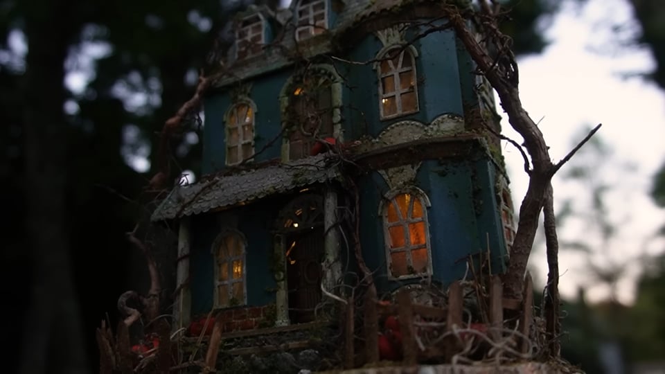 A close-up of a miniature dollhouse covered in vines and pumpkins