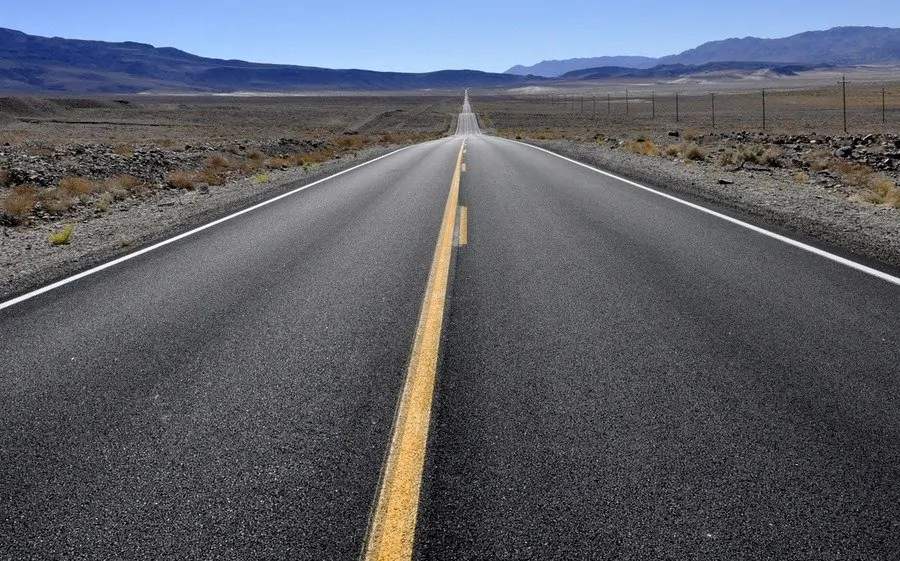 a road stretches off into the distance, either side is the desert of Death Valley