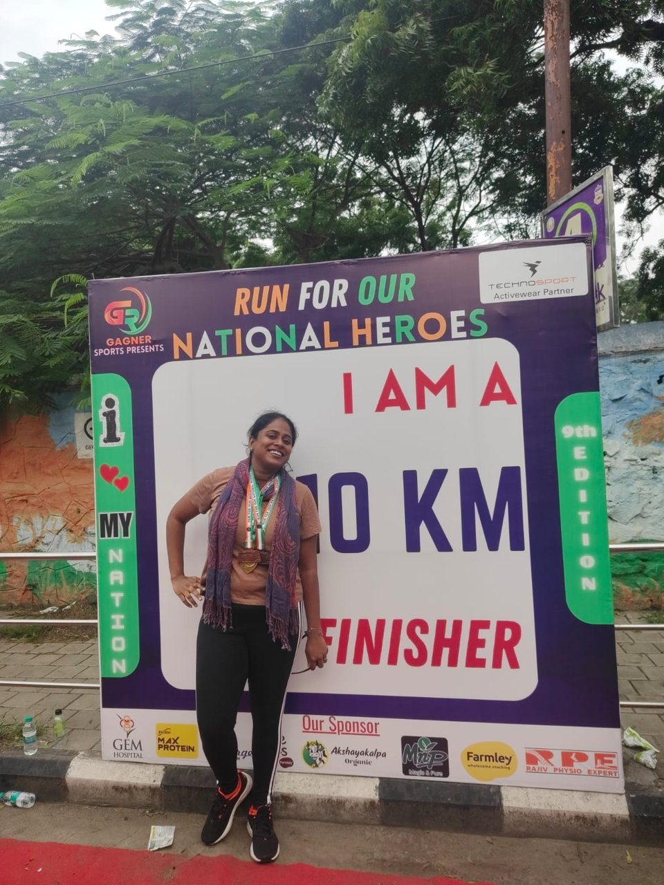Laasya poses in front of a "I AM A 10 KM FINISHER" billboard with medals