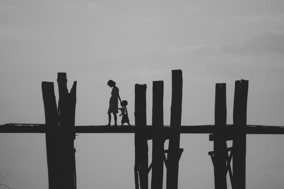 A Burmese woman walks with her child along an elevated wooden walkway