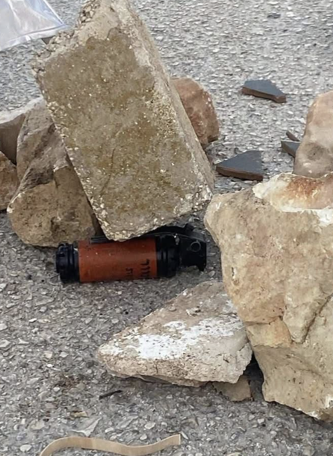 A pile of stones, atop a brown and black canister with Hebrew writing