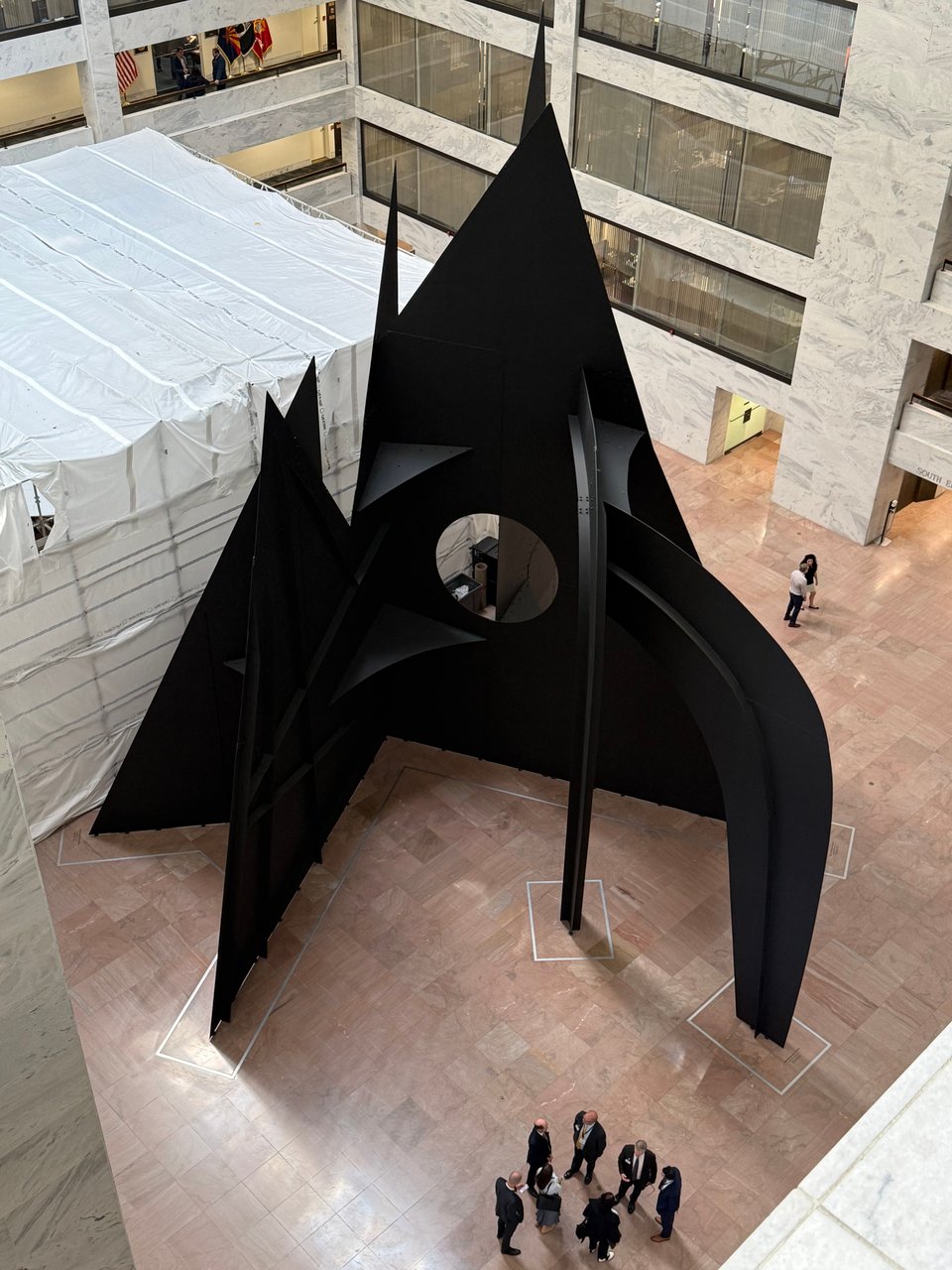 photo of the base of Alexander Calder's CLOUDS sculpture, showing a bunch of of metal planes and curves; it's situated in the lobby of the Senate Hart building, and the photo is taken from several floors up, and there are some people in suits near the sculpture