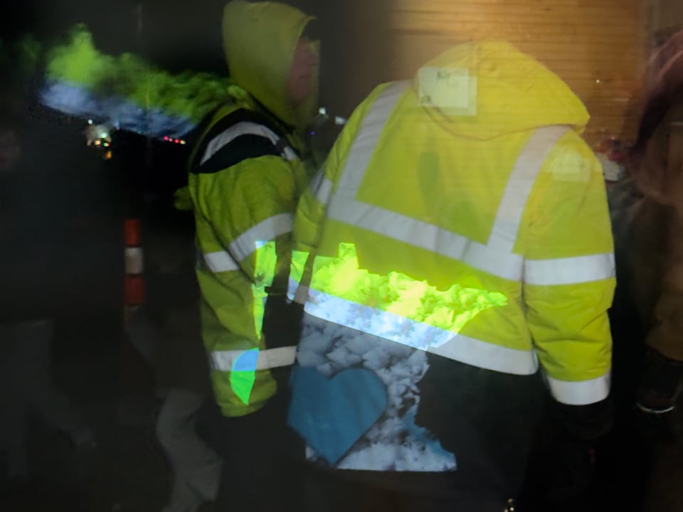 Workers in high-visibility clothing standing outside of a window, with the shape of Minnesota projected onto their clothing.