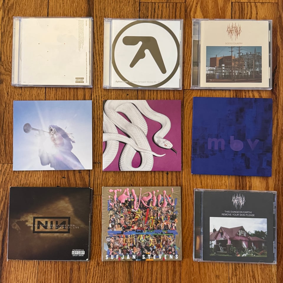 left to right/top to bottom: CDs of The 1975’s A Brief Inquiry into Online Relationships, Aphex Twin’s Selected Ambient Works Volume 1, Chat Pile’s God’s Country, Geese’s Getting Killed, Deftones’ private music, My Bloody Valentine’s m b v, Nine Inch Nails’ Live: And All That Could Have Been (been looking for this one for years!), Sufjan Steven’s Javelin, and Chat Pile’s This Dungeon Earth/Remove Your Skin Please.