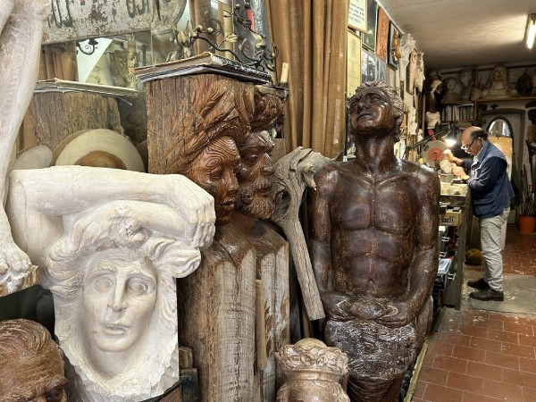 sculptor Franco Casoni working in his workshop surrounded by wooden sculptures of people and faces