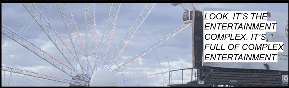 Part of a lit of Ferris Wheel next to a billboard. Text is imposed that reads "Look. It's the entertainment complex. It's full of complex entertainment."