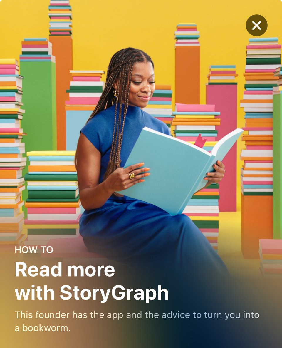 I'm pictured sitting against a colorful backdrop of towering stacks of books, smiling while reading a large blue book. I'm wearing a blue dress, and the setting is vibrant and playful. This promotional image highlights my creation, StoryGraph, and offers advice on becoming an avid reader, with personalized recommendations to match any reading mood.