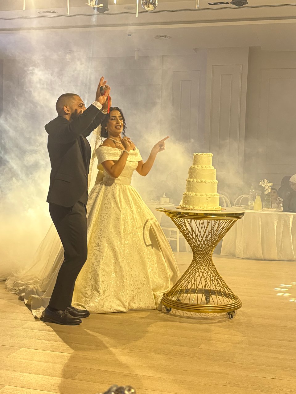 A man in a tuxedo and a woman in a wedding dress dancing in front of a tiered wedding cake