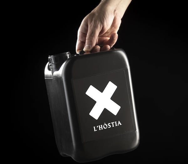 Un bidón rectangular de plástico negro sujetado por una mano sobre fondo negro. El bidón tiene aspecot de bidónd de gasolina. En el centro de la cara frontal del bidón, en letras blancas y tipografía historicista puede leeerse