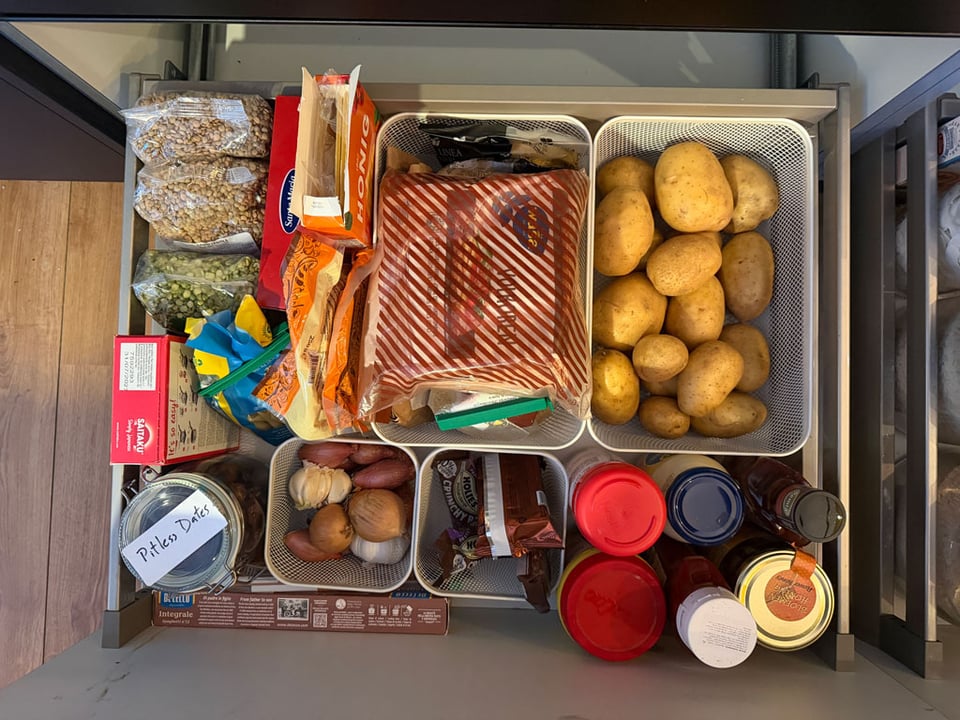 A kitchen drawer is organized with potatoes, sauces, lentils