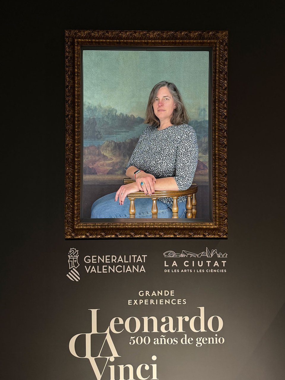 A woman sits in a frame with the background of Mona Lisa so that a photo can be taken as if she was La Gioconda