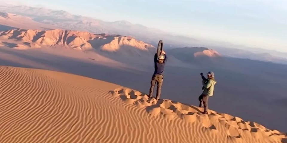 A man prepares to hurl a tire off a sand dune.