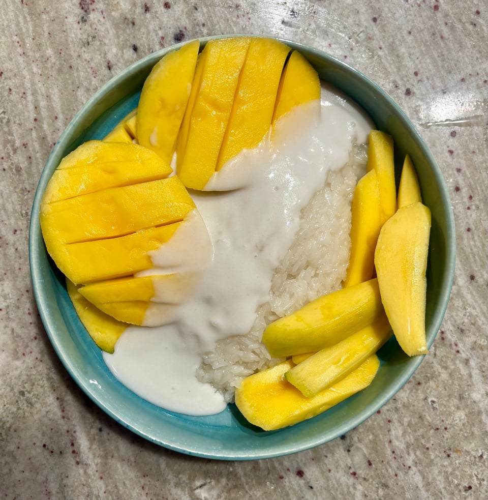 A blue plate of sliced mango on top of sticky rice with a coconut cream drizzled on top.
