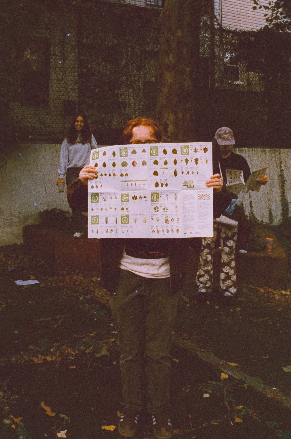 claire holds up the tree ID guide, with malka and dan in the background. from a warmer month.