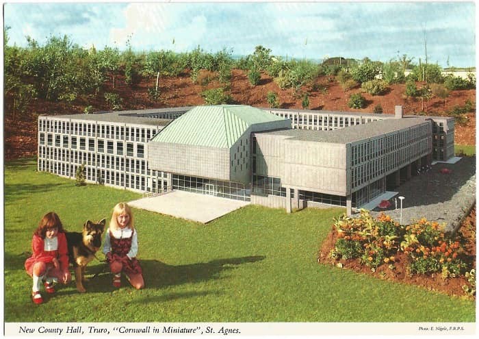 An overly processed postcard showing a model of Lys Kernow. Two girls and a German Shepard dog sit in front of it.