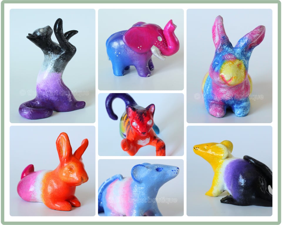 A collage of colorful animal figurines: A playful cat batting at the air painted in the ace pride colors, a cat in the same pose seen from above painted in rainbow colors, a bi pride elephant, a pan pride loafing rabbit, a lesbian pride loafing rabbit, a trans pride rat, and a nonbinary pride rat.

The shop name, the beast boutique, watermarks the image.