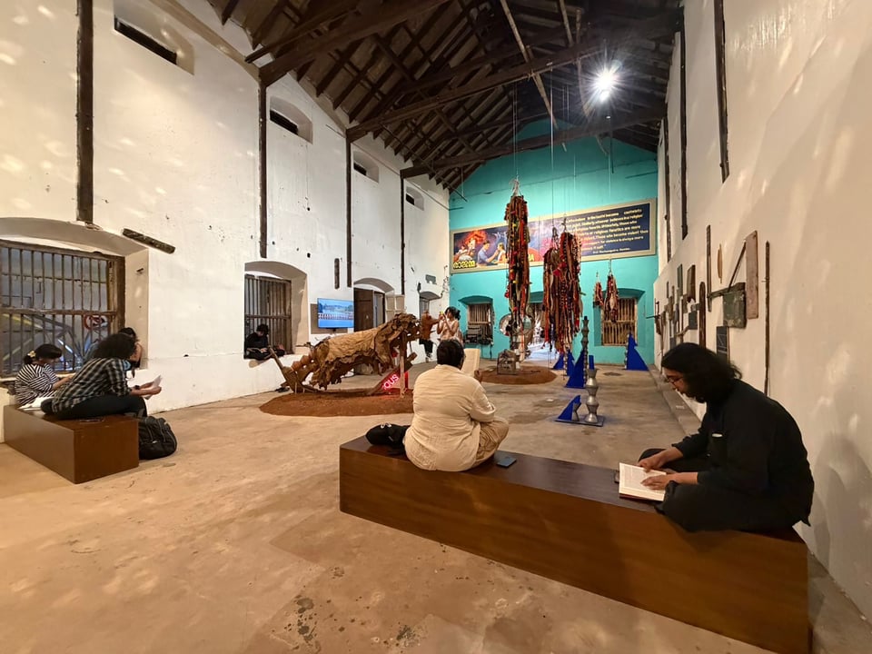 A group of people sitting and reading in the context of an art installation by Prabhakar Kamble in a warehouse at Kochi Biennale.